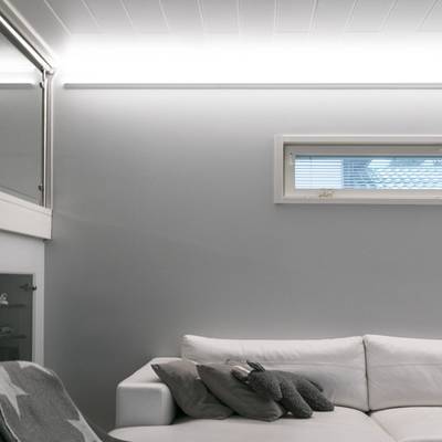 Un salón minimalista con luz natural, cortinas en las ventanas y una suave iluminación LED sobre paredes grises.