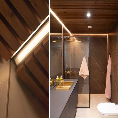 Un cuarto de baño moderno, iluminado con luz LED de techo, que resalta el mobiliario y los detalles de madera natural.
