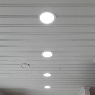 Cuatro plafones LED empotrables iluminan una habitación con paneles blancos. Los paneles LED redondos iluminan con un haz amplio.