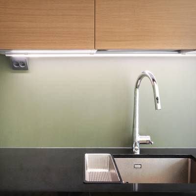 Fregadero de cocina con iluminación LED, grifo cromado, encimera negra y retroiluminación verde claro bajo el mueble.