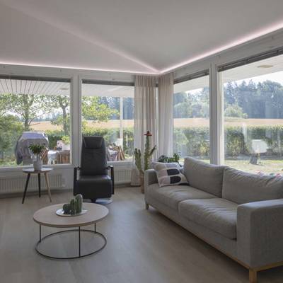Moderna sala de estar con lámparas LED de techo, lámpara de pie, luz natural de grandes ventanales, cómodos asientos.