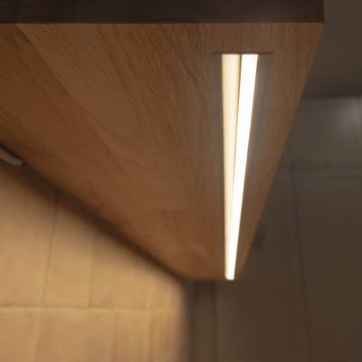 La tira de luces LED situada debajo de la estantería de madera proyecta sobre la pared una luz indirecta y cálida, ideal como iluminación de acento