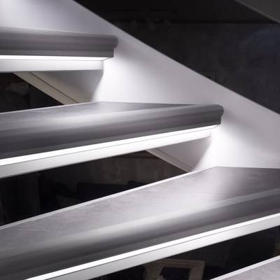 Vista detallada de una escalera flotante con una elegante luminaria LED, iluminación de acento y una pared blanca.