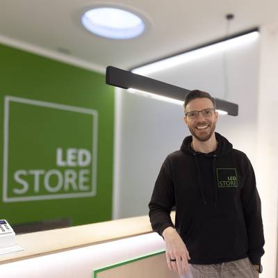 Un hombre en LED STORE-huvtröja vid belysningsdisk, green LED-skylt, ambiente moderno de boutique
