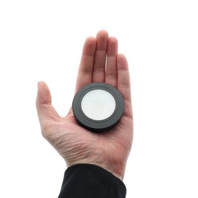 La mano muestra un downlight LED circular con difusor blanco y borde negro sobre fondo blanco liso.