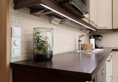La iluminación LED bajo el armario ilumina la encimera de la cocina, que alberga el terrario, el fregadero, el grifo y los electrodomésticos.