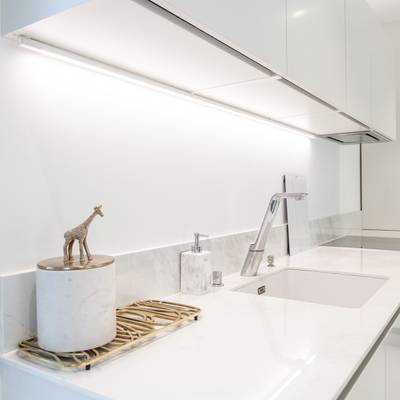 Cocina moderna con encimera blanca, grifo plateado, figura de jirafa en la cuba; iluminación LED brillante bajo los armarios para ganar espacio.