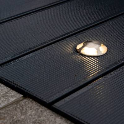 Luz de cubierta redonda de color plateado con tablas de madera estriadas oscuras, que emite un suave resplandor por la noche. Ideal para soluciones de iluminación LED para exteriores.