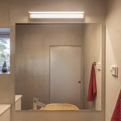 Baño moderno con iluminación LED de bajo consumo, espejo grande, encimera beige, grifo elegante y toallero rojo para un interior con estilo.