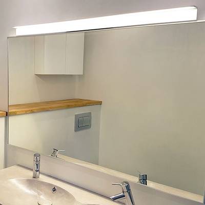 Cuarto de baño con espejo iluminado con LED, lavabo y grifería modernos, estante de madera y armarios blancos. La solución de iluminación ideal de la tienda de iluminación LED.