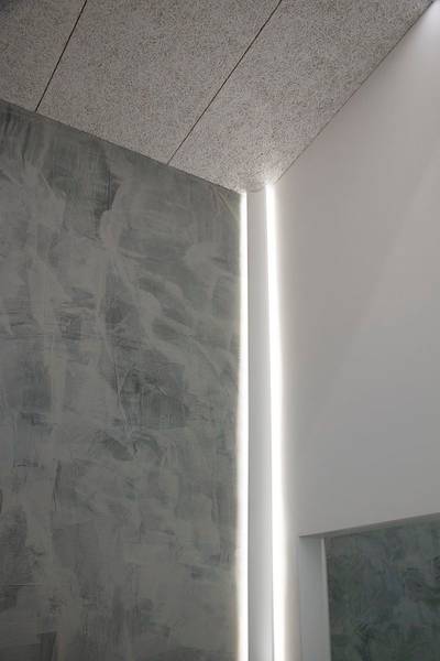Una pared gris texturizada se une a una pared blanca lisa con una tira de luz LED vertical.