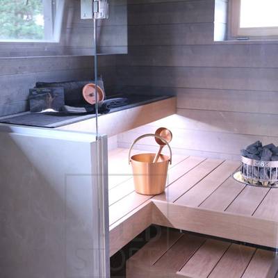 Interior de sauna moderna con bancos de madera, puerta de cristal, depósito de agua de cobre en el suelo y piedras calefactoras en la esquina. Ideal para mejorar la iluminación LED.