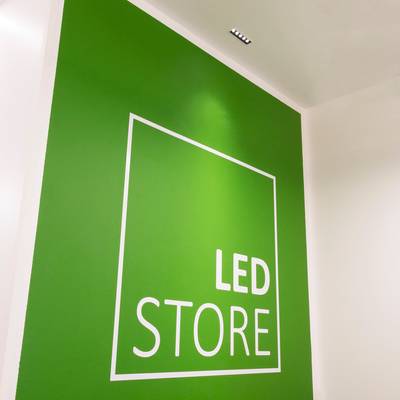 Texto alternativo: 'Pared verde con 'LED STORE' contorno cuadrado blanco, letras en negrita, luces de techo