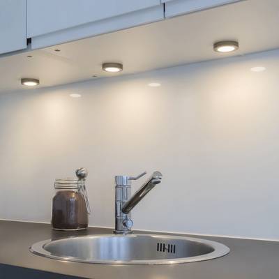 Tres luces LED bajo el armario iluminan el salpicadero cerca del moderno grifo de la cocina y la jarra de cristal.