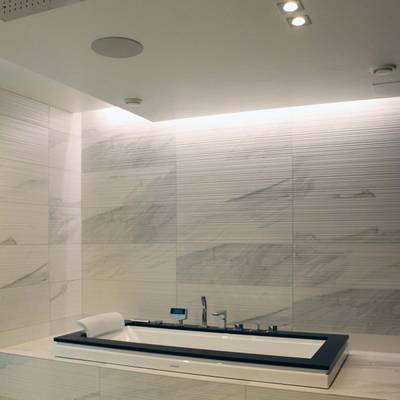 Baño moderno con azulejos de mármol, bañera rectangular y luces LED empotradas en el techo