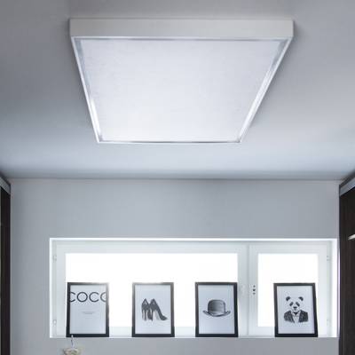 La luz LED de techo ilumina imágenes enmarcadas monocromas de texto, zapatos, sombrero y panda en una estantería junto a una ventana en el interior de una casa moderna.