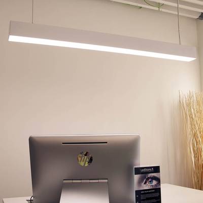 Una elegante lámpara LED de escritorio que ilumina una oficina moderna con un ordenador sobre un escritorio blanco; al fondo, ramas decorativas en un jarrón alto.