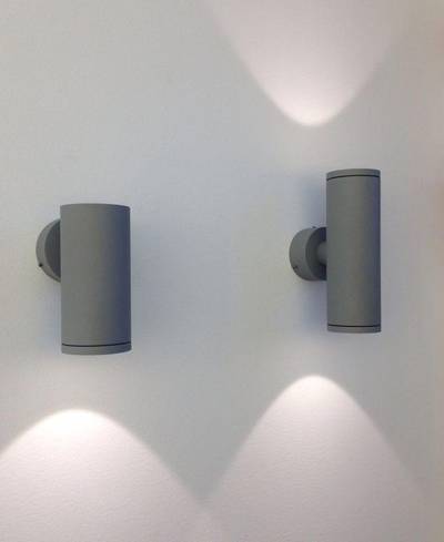 Los modernos apliques LED cilíndricos proyectan una suave luz ascendente y descendente sobre una pared blanca, creando un ambiente elegante en un diseño de iluminación contemporáneo.
