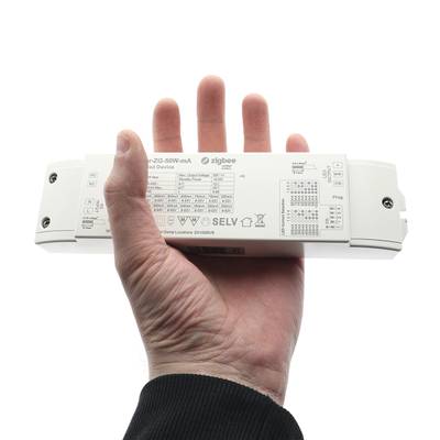 En la mano, un dispositivo rectangular blanco que muestra información técnica y símbolos y la palabra "Zigbee" asociada a la tecnología de iluminación LED.