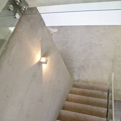 Una escalera moderna con peldaños de hormigón, balaustrada de cristal y luz LED montada en la pared que brilla cálidamente; el diseño minimalista contribuye al ambiente.