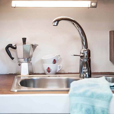 Moderno fregadero sobre encimera con grifo cromado, olla moka, tazas superpuestas con logotipo rojo, toalla azul claro sobre encimera: el lugar perfecto para la iluminación LED de bajo consumo.
