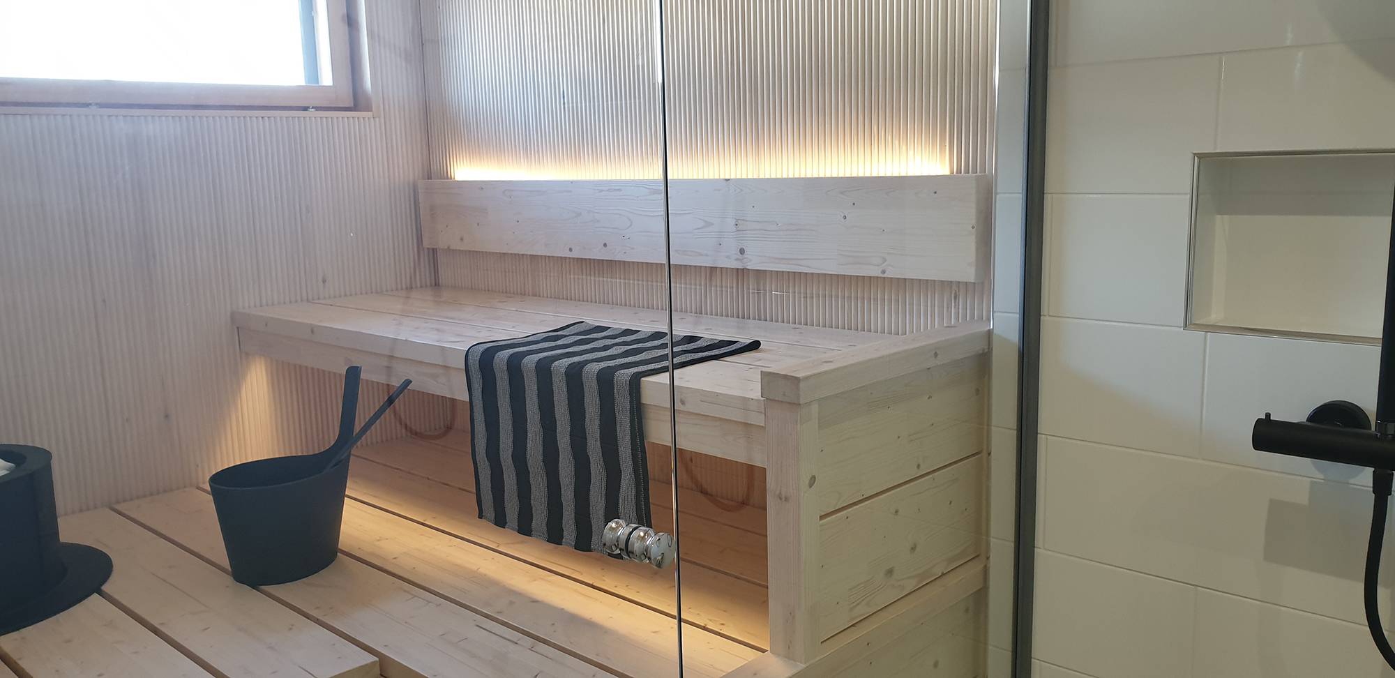 Una tira de LED en la parte posterior del respaldo de la sauna ilumina la luz atmosférica hacia arriba y hacia abajo por debajo del techo. Ledstore.fi