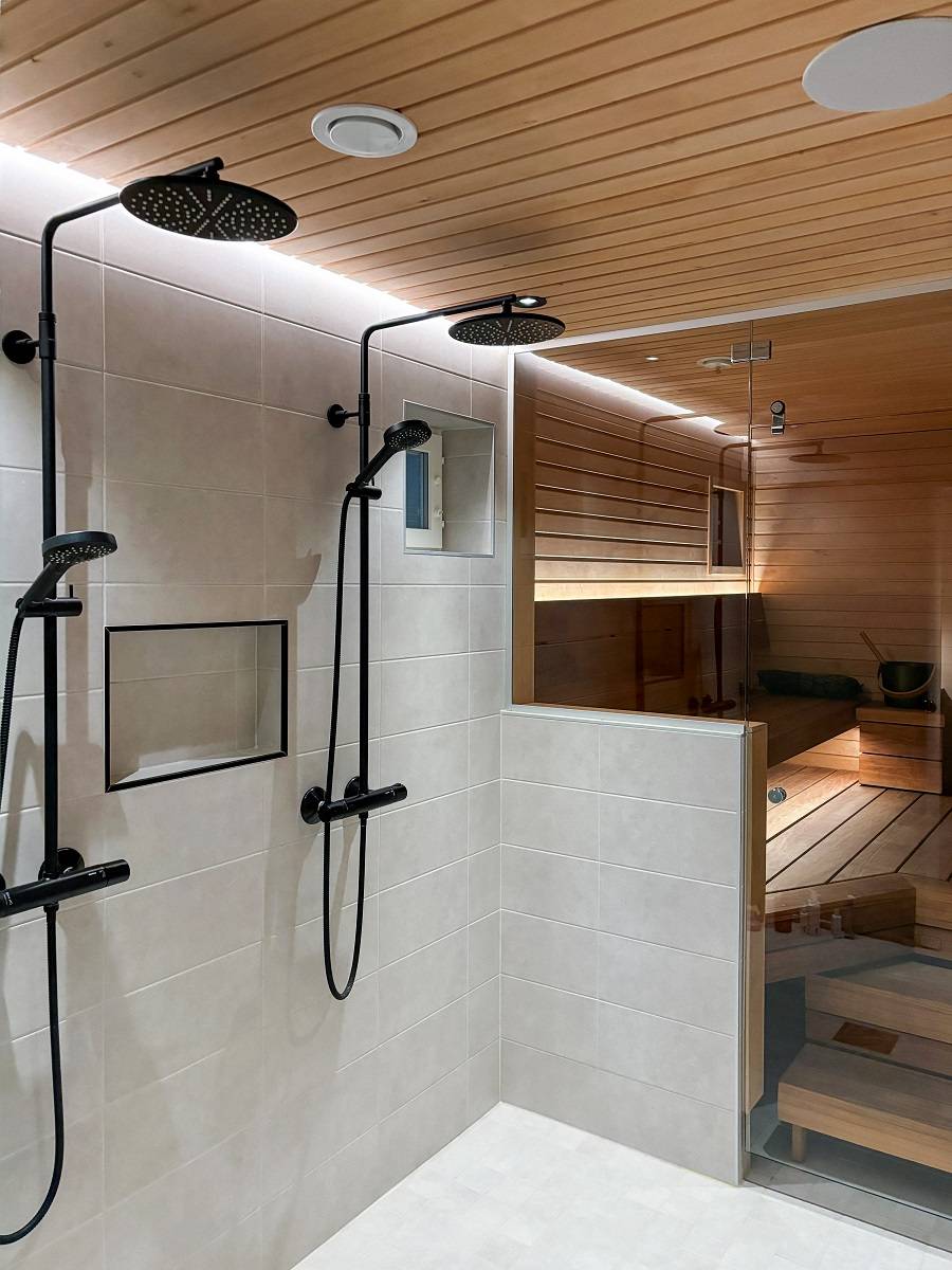 Detrás de las duchas, una tira de luz LED en una ranura en la línea del techo ilumina indirectamente a lo largo de la pared hasta el suelo. La luz es eficiente y agradable a la vista. © LedStore.fi