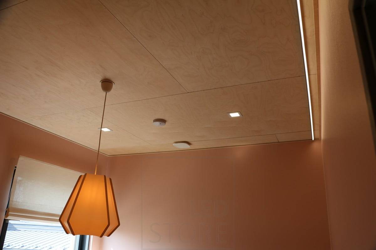 Feria de la Vivienda 2019: Pequeñas luces de panel en un techo de madera contrachapada. Tira led iluminando la pared para luz indirecta. Ledstore.fi