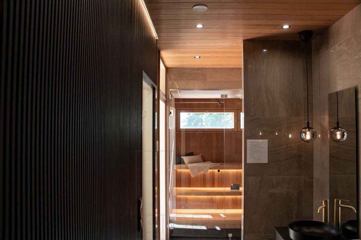 Feria de la Vivienda 2022: Iluminación atmosférica en el aseo y la sauna. La luz indirecta acentúa la pared de la cornisa y las tiras de LED bajo el techo de la sauna. Luz colgante como bello elemento decorativo. Ledstore.fi