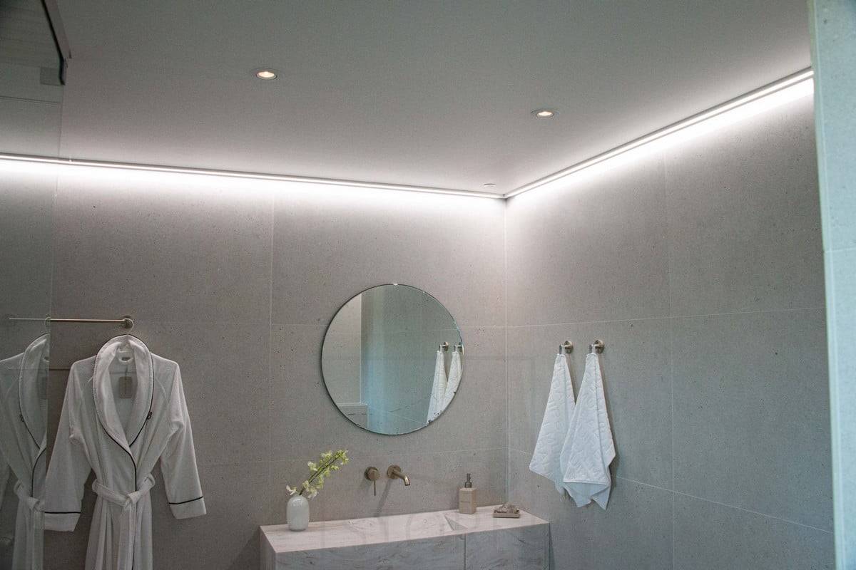 Housing Fair 2022: Tira de leds montada sobre una superficie de perfil bajo, en el techo junto a la pared, que proporciona una luz suave e indirecta para el cuarto de baño. Ledstore.fi
