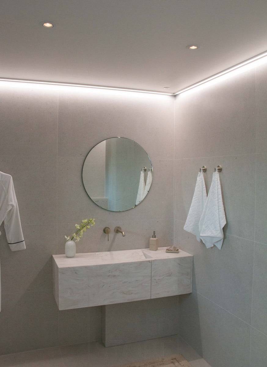 Housing Fair 2022: Tira de leds montada sobre una superficie de bajo perfil, en el techo junto a la pared, iluminando el baño con luz atmosférica. Ledstore.fi
