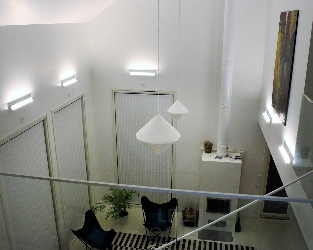 Una iluminación indirecta atmosférica para el salón con apliques Led BLADE. La luminaria está montada para iluminar desde abajo hacia arriba, por lo que la iluminación indirecta también enfatiza la altura del espacio y las obras de arte de la pared. Ledstore.fi