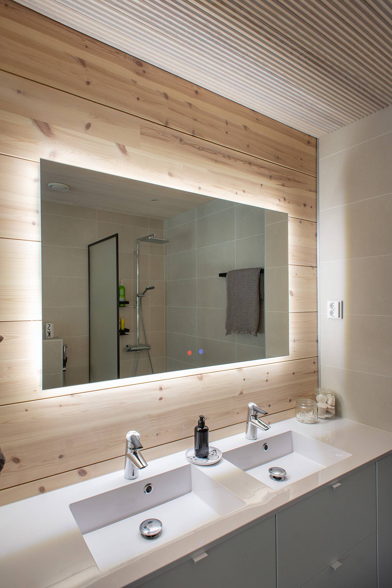 En el cuarto de baño, la luz de detrás de un espejo luminoso de 1200 mm x 750 mm resalta el bonito revestimiento de madera e ilumina el nivel. Ledstore.fi