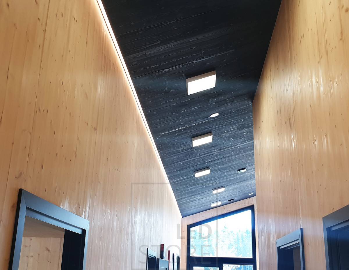 En un pasillo alto, una tira de LED entre el techo y la pared proporciona iluminación ambiental. Iluminación general con paneles luminosos. Ledstore.fi