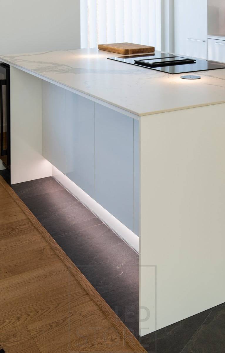 Tira de LED en el zócalo que acentúa la isla, creando luz indirecta en la cocina a través del suelo. Ledstore.fi