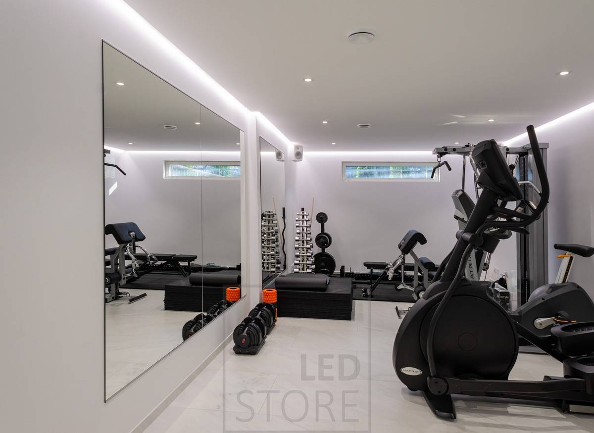 Gimnasio doméstico iluminado con focos y luz indirecta atmosférica. La iluminación indirecta se consigue con una tira de luz LED instalada entre el techo y la pared.