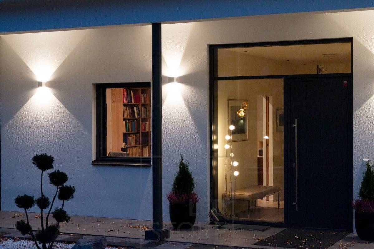 Apliques FUNK blancos en la pared del edificio, que iluminan la fachada y crean una iluminación atmosférica en el exterior. El ángulo de la luz es ajustable. Ledstore.fi