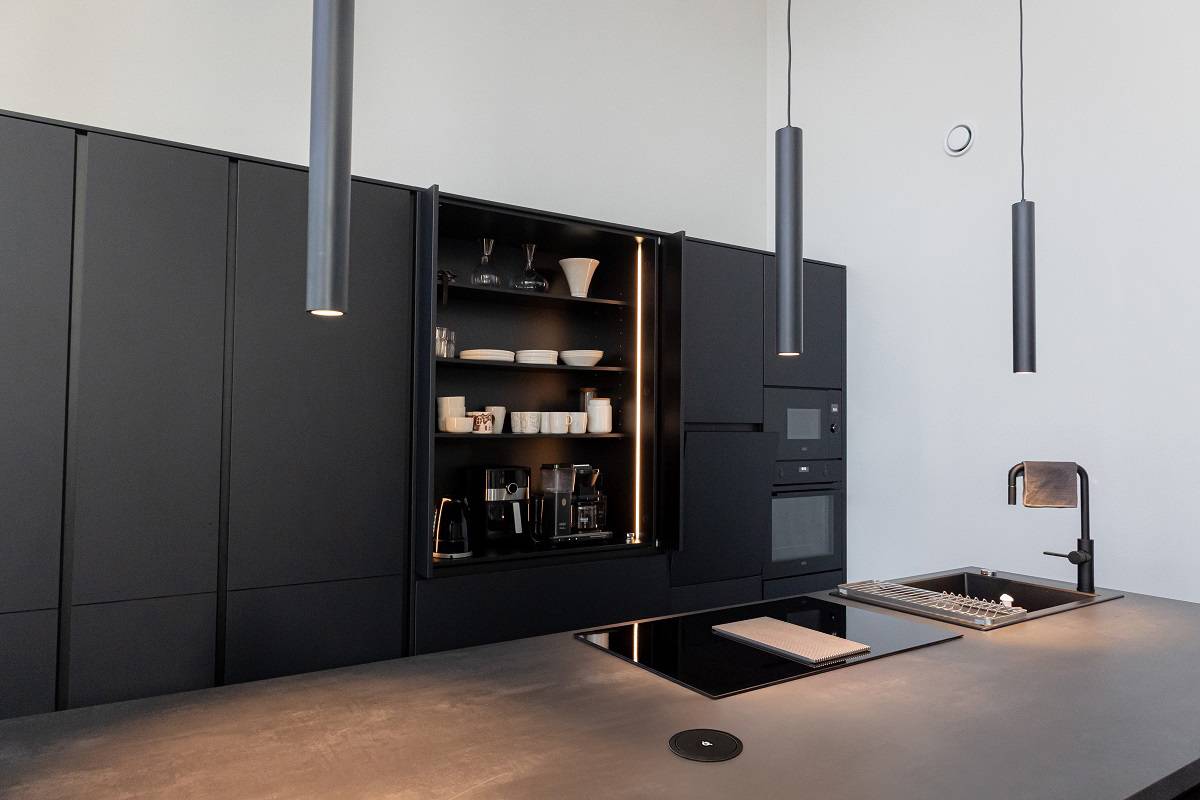 En la cocina hay tres lámparas colgantes negras PIIPPU 2.0 sobre la isla. Además, el armario del desayuno, situado detrás, está iluminado con una tira de LED instalada en vertical.