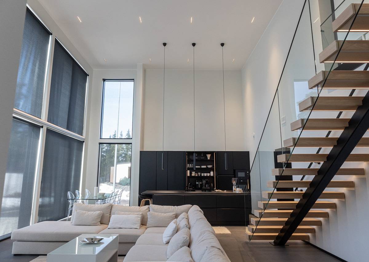 Focos LINJA10 para iluminación general en el techo alto del salón, la cocina y el comedor, y tres lámparas colgantes LED PIIPPU 2.0 sobre la isla de la cocina. Tira de LED en los peldaños de la escalera.