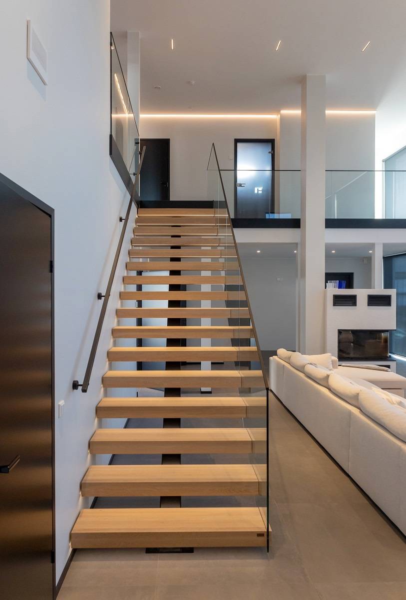 Escaleras de madera clara que conducen a la planta superior iluminadas por una tira de leds y una tira de leds que recorre la pared de la planta superior