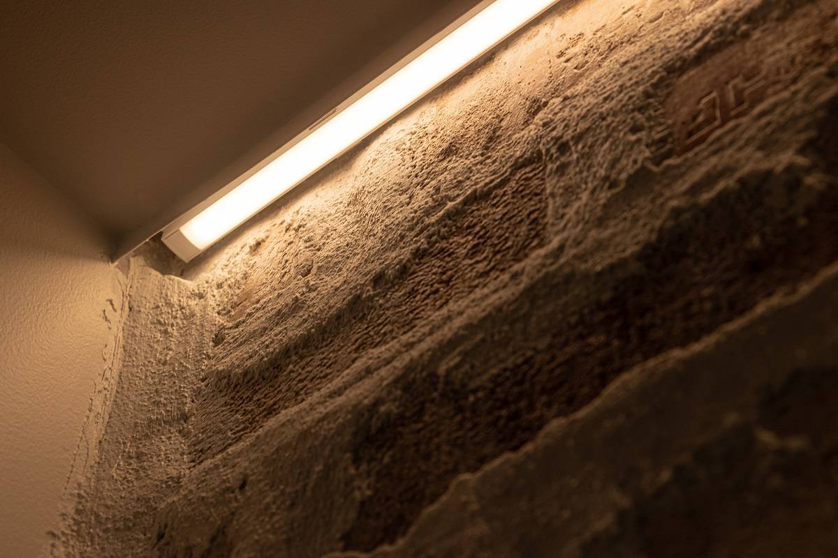 Primer plano de la instalación de una tira LED en una pared decorativa. La tira LED se ha instalado en un perfil de aluminio de montaje en superficie, situado entre el zócalo y la pared.