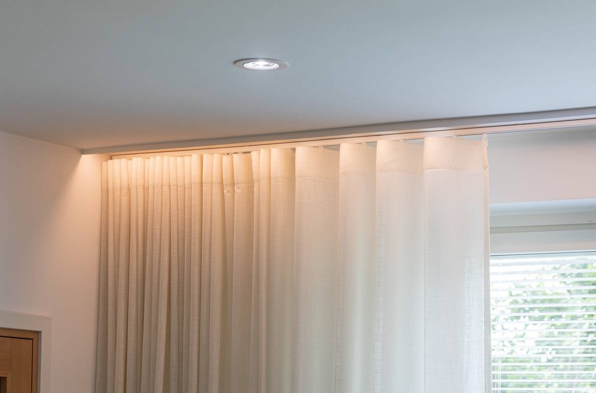 Luz descendente en el techo del salón. Delante de la cortina hay una tira de LED instalada detrás de la moldura, de modo que la fuente de luz queda oculta.