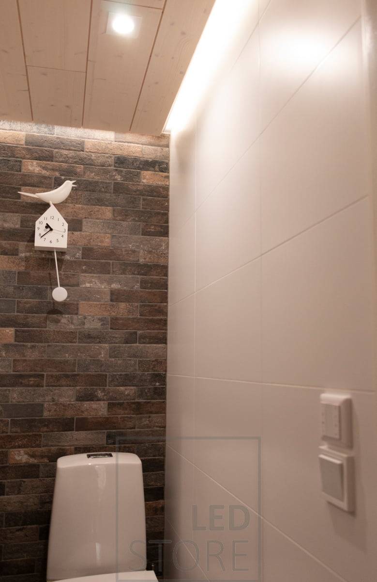 Iluminación puntual con downlight LED - LIGHT GREEN R023 e iluminación indirecta con perfil de superficie blanco en la ranura del techo con tira CCT de 7,2 W/m. En la pared también se ve un controlador inalámbrico montado encima del interruptor de la luz.