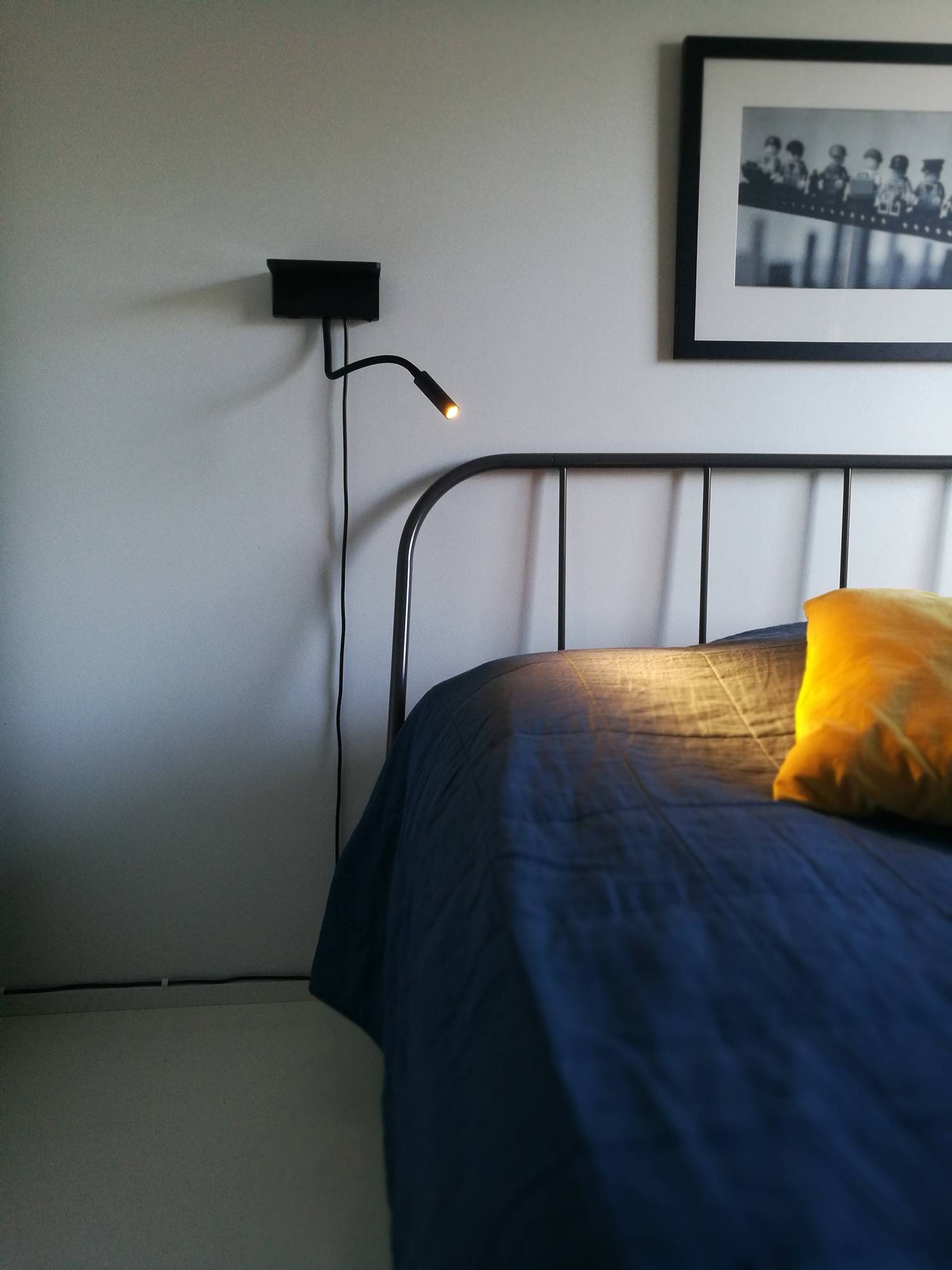 Lámpara de pared BLADE junto a la cama. Funciona como luz de lectura y dispone de carga fija e inalámbrica para el teléfono. Ledstore.fi