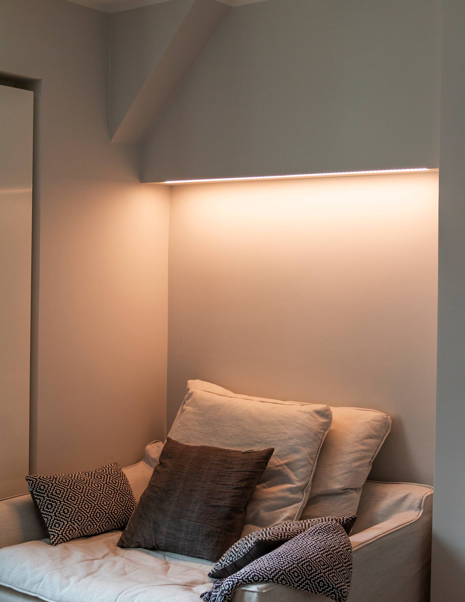 Dormitorio con iluminación ambiental controlada por temperatura de color encima de la cama, tira de leds montada en la parte inferior del mueble en una superficie de perfil bajo. La luz tiene un tono cálido en la imagen. Ledstore.fi