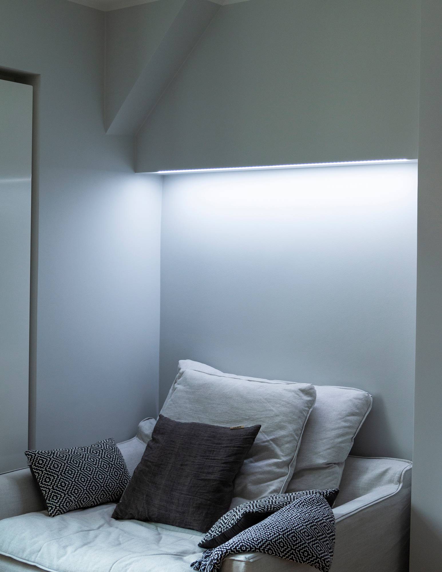 Dormitorio con iluminación ambiental regulable en temperatura de color detrás de la cama, montada en la base del armario. En la imagen, la temperatura de color está ajustada a un tono frío. Ledstore.fi