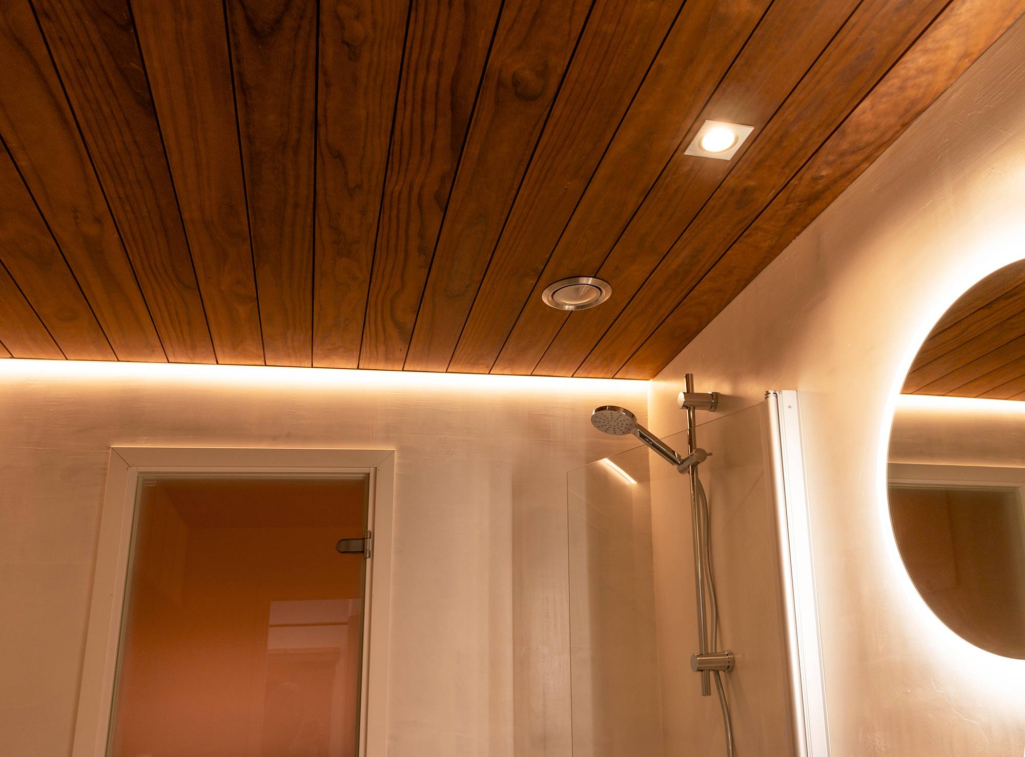 Perfil de borde con tira led iluminando la ducha combinado con un espejo de luz y maceteros de techo. Ledstore.fi