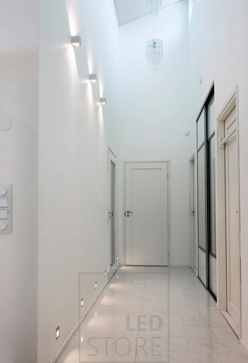 Apliques led empotrables IN-WALL que crean luz indirecta en el pasillo a ras de suelo. Sobre ellos, apliques led CUBIC que iluminan en dos direcciones, resaltando la altura del espacio. Ledstore.fi