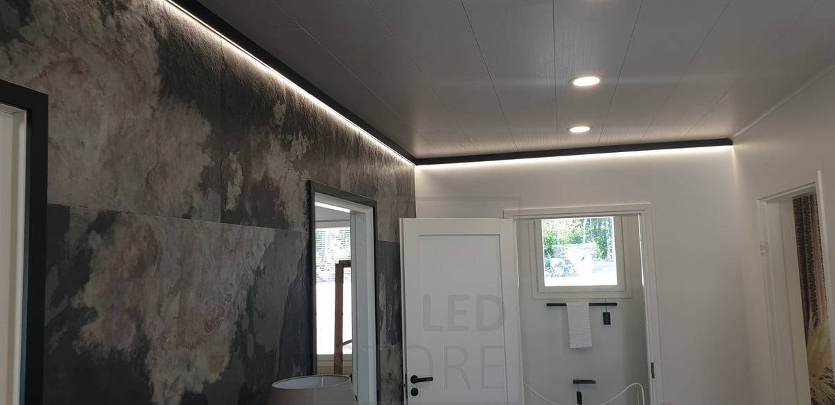 Un decorativo y lineal perfil de pared negro con una tira de luz LED que proporciona luz indirecta. Ledstore.fi