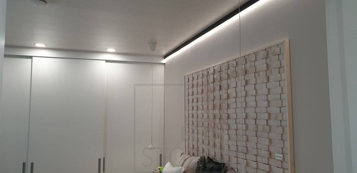 Un perfil de pared negro en el borde del tejado sustituyendo a un listón de tejado. Tira de luz led que brilla hacia abajo para iluminar indirectamente a través de la pared. Ledstore.fi